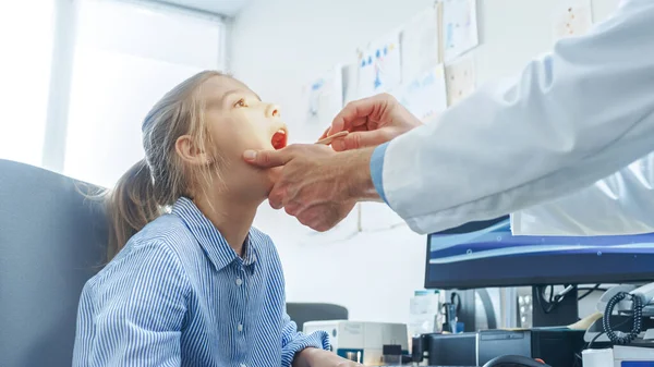 Amistoso médico comprueba las niñas dolor de garganta, curación de la gripe. Atención médica moderna, pediatra amigable y oficina brillante. —  Fotos de Stock