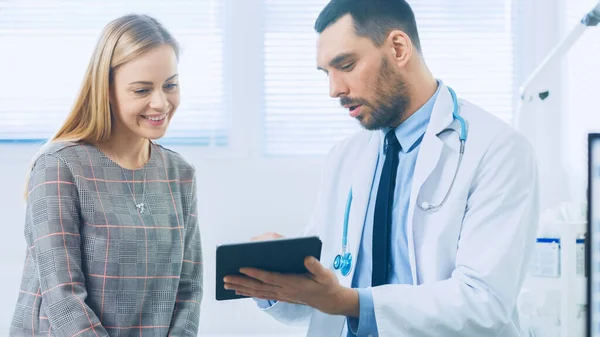 Schöne Frau besucht Arztpraxis, er zeigt Tablet-Computer mit ihrer Krankengeschichte, sie besprechen ihre Gesundheit und andere medizinische Fragen. Moderne Arztpraxis. — Stockfoto