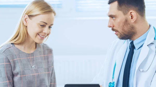 Schöne Frau besucht Arztpraxis, er zeigt Tablet-Computer mit ihrer Krankengeschichte, sie besprechen ihre Gesundheit und andere medizinische Fragen. Moderne Arztpraxis. — Stockfoto