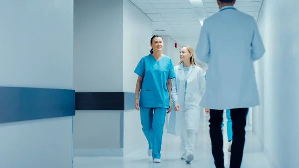 Женщина-хирург и женщина-доктор прогуливаются по больничному коридору, говоря о здоровье пациентов. Современная светлая больница с профессиональным персоналом. — стоковое фото