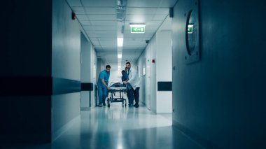 Emergency Department: Doctors, Nurses and Surgeons Push Gurney Stretcher with Seriously Injured Patient towards the Operating Room. Light Dramatically Turns on. clipart