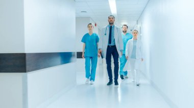 Doktorlar, Cerrahlar ve Hemşireler Ekibi Yoğun Hastane Koridorunda yürüyor, Hastalar, Yaklaşan Ameliyatlar ve Hayatları Kurtarma hakkında konuşuyorlar. Profesyonel Personelle Temiz Modern Hastane.