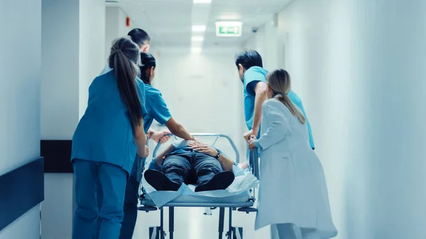 Τμήμα Επειγόντων Περιστατικών: Γιατροί, Νοσοκόμες και Νοσηλευτές σπρώχνουν το φορείο με σοβαρά τραυματισμένο ασθενή προς το χειρουργείο. Φωτεινό σύγχρονο νοσοκομείο με επαγγελματικό προσωπικό που σώζει ζωές. — Φωτογραφία Αρχείου