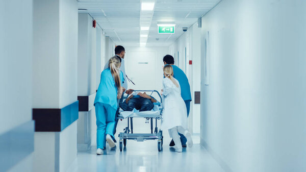 Emergency Department: Doctors, Nurses and Paramedics Push Gurney Stretcher with Seriously Injured Patient towards the Operating Room. Bright Modern Hospital with Professional Staff Saving Lives.