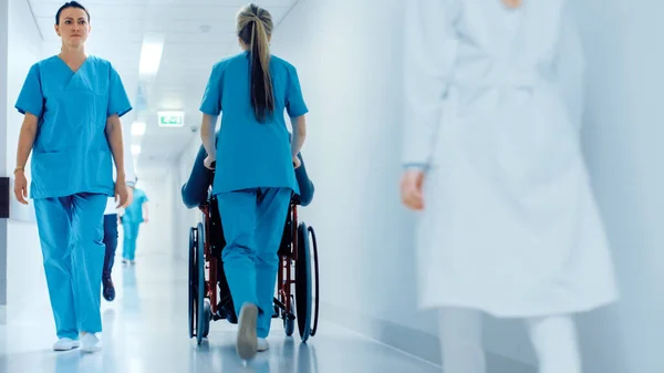 Postřelen ženskou sestrou pohybující se pacientkou v invalidním vozíku nemocniční chodbou. Dělat procedury. Bright Modern Hospital with Friendly Staff. — Stock fotografie