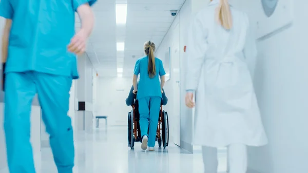 Tiro da enfermeira paciente em movimento na cadeira de rodas através do corredor do hospital. A fazer procedimentos. Hospital moderno brilhante com funcionários amigáveis. — Fotografia de Stock