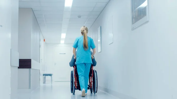 Aufnahme einer Krankenschwester, die eine Patientin im Rollstuhl durch den Krankenhausflur bewegt. Vorgehensweise. Helles modernes Krankenhaus mit freundlichem Personal. — Stockfoto