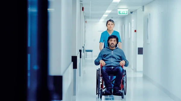 Kvinnlig sjuksköterska Pushing Patient i rullstolen Genom sjukhuset korridoren, De går till procedurer. Ljusa moderna sjukhus med vänlig personal. — Stockfoto