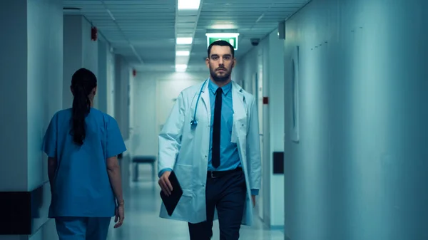 Médico bonito determinado vestindo casaco branco com estetoscópio caminha através do corredor do hospital. Clínica brilhante moderna com equipe profissional. — Fotografia de Stock