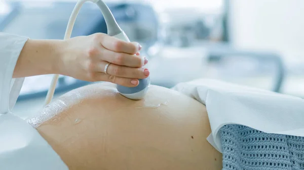 Im Krankenhaus, Nahaufnahme des Arztes, der einer schwangeren Frau eine Ultraschalluntersuchung vornimmt. Geburtshelferin bewegt Schallwandler auf dem Bauch der zukünftigen Mutter. — Stockfoto