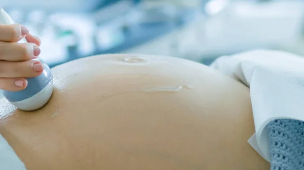 Im Krankenhaus, Nahaufnahme des Arztes, der einer schwangeren Frau eine Ultraschalluntersuchung vornimmt. Geburtshelferin bewegt Schallwandler auf dem Bauch der zukünftigen Mutter. — Stockfoto