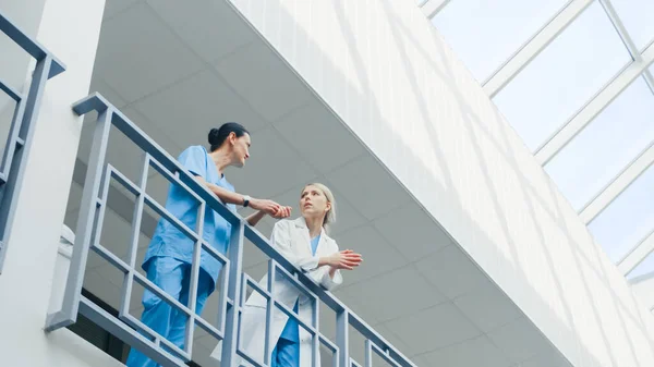 Lage hoek schot van de tweede verdieping ziekenhuis interieur, verpleegkundige en arts bespreken dringende gezondheid gerelateerde zaken. Beroepsbeoefenaren. — Stockfoto