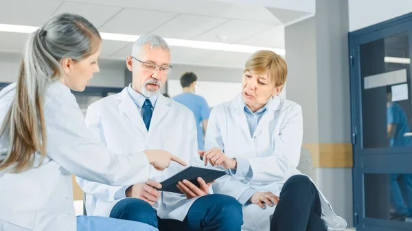病院のロビーでは、 3人の専門医が座りながらディスカッションをします。タブレットPCを使用しています。国で最高の専門家や医療機関と忙しい現代病院. — ストック写真