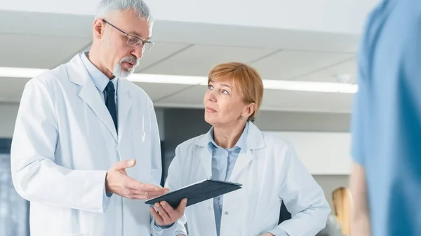 På sjukhuset Läkare har Diskussion medan du använder Tablet Computer. I bakgrunden patienter och medicinsk personal. Ny modern fullt fungerande medicinsk anläggning. — Stockfoto