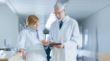 Hastanedeki iki doktor resepsiyon masasında duruyor, Tablet Bilgisayar hakkında konuşuyor ve bilgi paylaşıyorlar. Hastalar ve Tıbbi Personelle Modern Hastane.