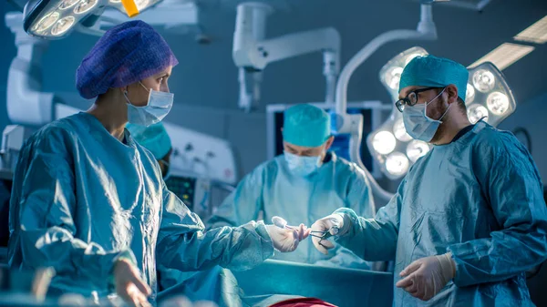 Olika team av professionella kirurger utför invasiv kirurgi på en patient i sjukhusets operationssal. Sjuksköterska Hands Out Instrument till kirurg, narkosläkare Övervakar värden. Verklig modern — Stockfoto