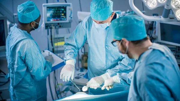 Команда професійних хірургів, асистентів та медсестер виконують інвазивну хірургію пацієнта в операційній кімнаті лікарні. Хірург користується інструментами. Справжня сучасна лікарня з автентикою — стокове фото