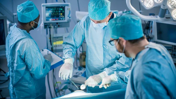 Equipo Diverso de Cirujanos Profesionales, Asistentes y Enfermeras que Realizan Cirugía Invasora a un Paciente en la Sala de Operaciones del Hospital. Instrumentos de uso de cirujanos. Real Hospital Moderno con Auténtico —  Fotos de Stock