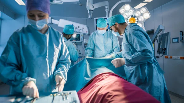 Zróżnicowany zespół profesjonalnych chirurgów, asystentów i pielęgniarek wykonujących operacje inwazyjne na pacjencie w sali operacyjnej szpitala. Chirurdzy rozmawiają i używają instrumentów. Real nowoczesny szpital z — Zdjęcie stockowe