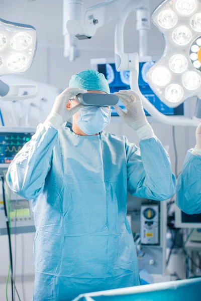 Chirurgen setzen eine Augmented-Reality-Brille auf, um im High-Tech-Krankenhaus hochmoderne Operationen durchzuführen. Ärzte und Assistenten arbeiten im Operationssaal. — Stockfoto