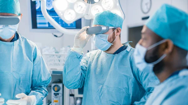 Surgeons Wearing Augmented Reality Glasses Perform State of the Art Augmented Reality Surgery in High Tech Hospital. Doctors and Assistants Working in Operating Room.
