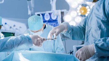 Ameliyathanede yakın çekim, Asistan ameliyat sırasında cerrahlara ekipman dağıtıyor. Ameliyat devam ediyor. Profesyonel Tıp Doktorları Ameliyat Yapıyor.