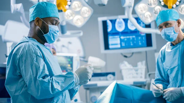 Portrait of the Black Professional Surgeon Performing Invasive Surgery on a Patient in the Hospital Operating Room. In the Background Modern Hospital Operating Room.