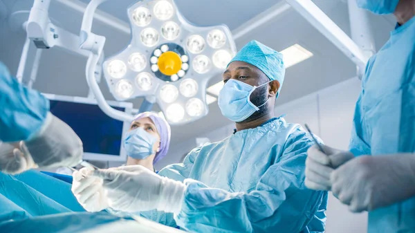 Diverse Team of Professional surgeon, Assistants and Nurses Performing Invasive Surgery on a Patient in the Hospital Operating Room. Surgeons Talk and Use Instruments. Real Modern Hospital with