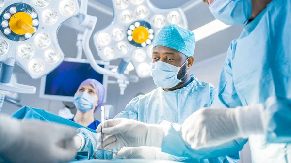 Équipe diversifiée de chirurgiens professionnels, d'adjoints et d'infirmières pratiquant une chirurgie invasive sur un patient dans la salle d'opération de l'hôpital. Les chirurgiens parlent et utilisent des instruments. Hôpital moderne réel avec — Photo