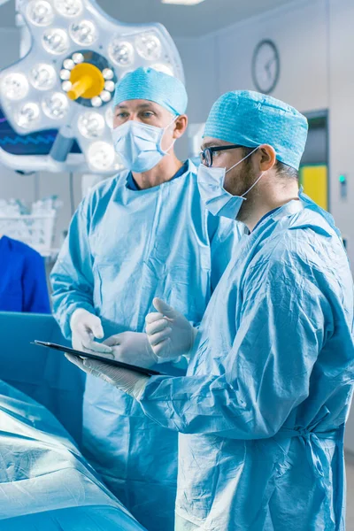 전문 외과의사와 보조 강연의 수직적 인 샷 그리고 수술중 디지털 태블릿 컴퓨터를 사용 한다. 현대 병원 운영 실에서 일하는 사람들. — 스톡 사진