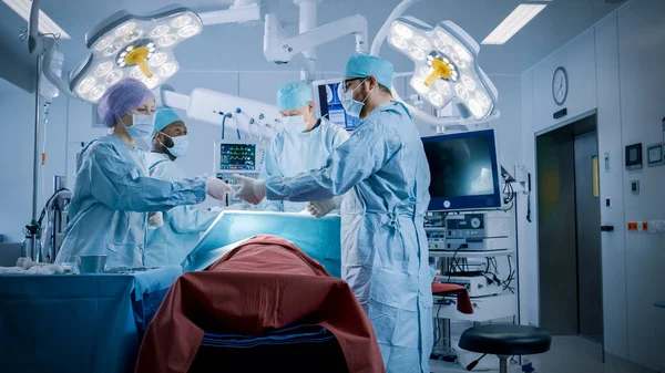 専門外科医の多様なチームは、病院の手術室で患者に侵襲手術を行う。看護師は外科医に機器を渡します,麻酔科医はバイタルを監視します.現代病院 — ストック写真