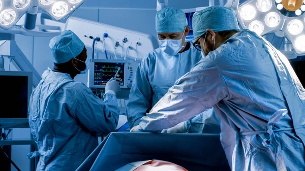 전문 외과의사의 Diverse Team of Professional Surgeons Performing Inusual Surgery on the Hospital Operating Room. 간호사는 외과의사, 마취과 의사, 모니터 바이탈에게 기기를 나눠 준다. 춥고 푸르다 — 스톡 사진