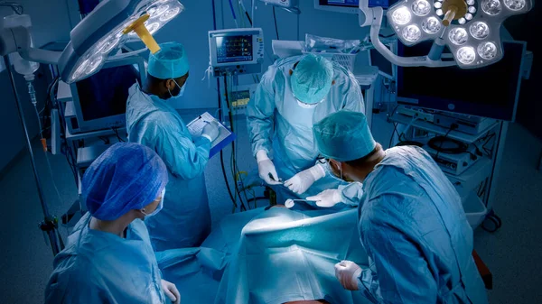 Prise de vue à grand angle d'une équipe diversifiée de chirurgiens professionnels, d'assistants et d'infirmières pratiquant une chirurgie invasive sur un patient dans la salle d'opération de l'hôpital. Véritable hôpital moderne avec équipement authentique. — Photo