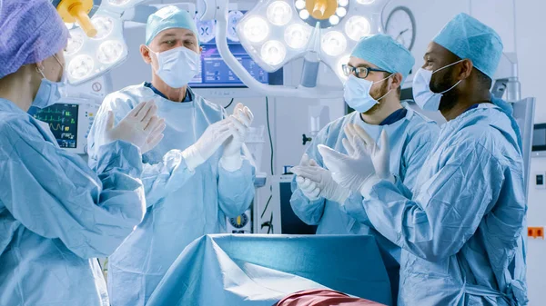I sjukhusets operationssal olika team av professionella kirurger och assistenter förväntar sig avslutad kirurgi och applådera framgångsrika resultat. Professionella läkare firar framgångsrikt räddat liv. — Stockfoto