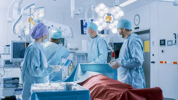 Equipo Diverso de Cirujanos Profesionales, Asistentes y Enfermeras que Realizan Cirugía Invasora a un Paciente en la Sala de Operaciones del Hospital. Los cirujanos hablan y usan instrumentos. Real Hospital Moderno con —  Fotos de Stock