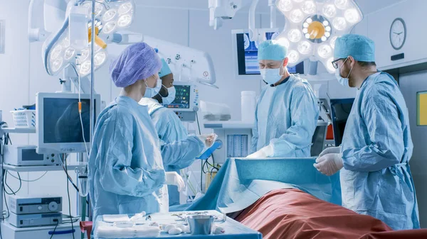 Equipo Diverso de Cirujanos Profesionales, Asistentes y Enfermeras que Realizan Cirugía Invasora a un Paciente en la Sala de Operaciones del Hospital. Los cirujanos hablan y usan instrumentos. Real Hospital Moderno con —  Fotos de Stock
