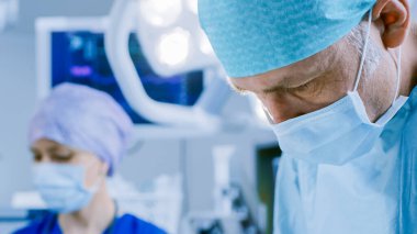 Profesyonel bir cerrahın yakın çekimi cerrahi bir operasyon yürütüyor. Arkaplanda Modern Hastane Operasyon Odası.