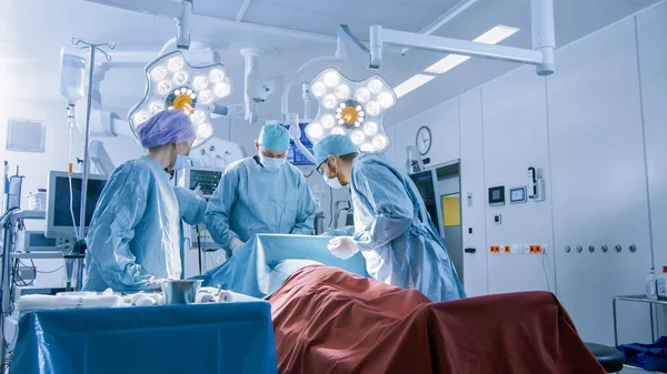 Aufnahme eines Teams professioneller Chirurgen, das invasive Operationen an einem Patienten im Operationssaal des Krankenhauses durchführt. Anästhesist überwacht Vitaldaten. Modernes Krankenhaus. — Stockfoto