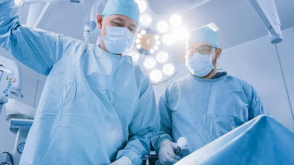 Disparo de ángulo bajo en el quirófano de dos cirujanos durante el procedimiento quirúrgico Inclinación del paciente con instrumentos. Médicos profesionales en un hospital moderno —  Fotos de Stock