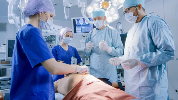 En el quirófano del hospital el anestesiólogo aplica la máscara de anestesia a un paciente, los asistentes desinfecta con el lugar de la incisión del yodo, los cirujanos esperan para comenzar la cirugía. —  Fotos de Stock