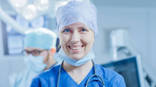 Portrait of the Professional Nurse Medical Assistant Removed Surgical Mask after Successful Operation. In the Background Modern Hospital Operating Room.