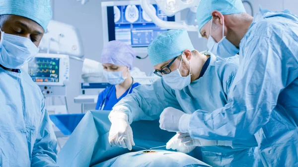 Professioneller Chirurg steht mit Chirurgenmaske und bereitet eine Spritze für die Injektion vor. Im Hintergrund moderner Krankenhaus-Operationssaal mit laufenden Operationen. — Stockfoto