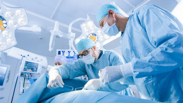 Inyección en ángulo bajo de un equipo diverso de cirujanos profesionales que realizan cirugía invasiva a un paciente en el quirófano del hospital. Los cirujanos utilizan instrumentos —  Fotos de Stock