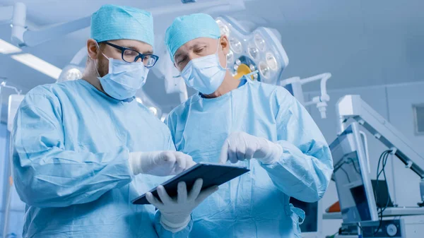 Dos cirujanos profesionales utilizan la computadora digital de la tableta mientras que están parados en la sala de operaciones moderna del hospital. —  Fotos de Stock