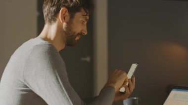 Dahili Ofis Stüdyosunda oturan Profesyonel Yaratıcı Adam Akıllı Telefon Kullanan Adam, Cep Telefonu Kullanan Adam, İnternet, Sosyal Ağ Medyası, Laptop 'ta çalışan. Kamera Hareket Ediyor