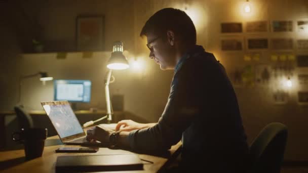 Professional Man Sitting at His Desk in Office Studio Working on a Laptop in the Evening. Man working with Data, Analyzing Statistics, writing Down Information. 360 Degree Tracking Arc Shot Movement — Stock Video