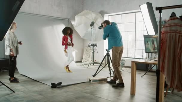 Backstage of the Photo Shoot : Make-up Artist Applies Makeup on Beautiful Black Model, in a Moment Le photographe commence à prendre des photos avec un appareil photo professionnel. Magazine de mode Studio Photoshoot — Video