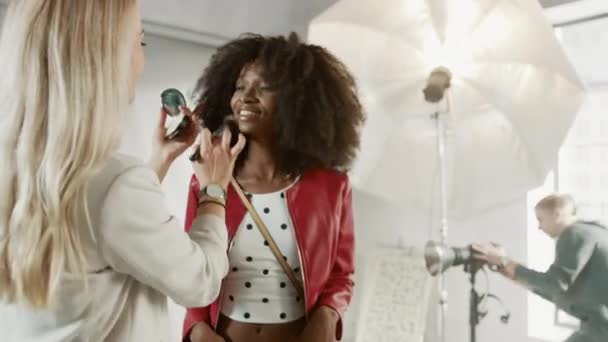 Zákulisí focení: make-up umělec aplikuje make-up na mladé krásné černošky model, v okamžiku fotograf začíná fotografovat s profesionální kamerou. Obal časopisu Fashion Photoshoot — Stock video