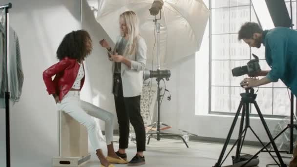Backstage of the Photo Shoot: Make-up Artist Apply lipstick Makeup on Beautiful Black Model, in a Moment Photographer Starts Taking Photos with Professional Camera. Revista de moda Studio — Vídeo de Stock