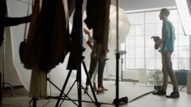 Fotoğraf çekiminin sahne arkası: Makyöz, gür kıvırcık saçlı güzel siyah modele ruj sürüyor. Çeşitli Tarz Pozisyonlarında Kız Duruyor. Moda Dergisi Stüdyo Fotoğrafları